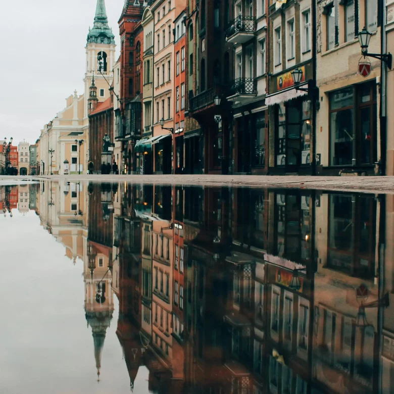 Rynek polskiego miasta z odbijającą się w kałuży nieruchomością oferowaną do najmu przez fundację rodzinną.